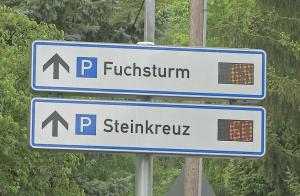 Schilder an einem Pfal die den Weg zu den Parkplätzen Fuchsturm und Steinkreuz, mit der Angabe der aktuellen Parkplätze, anzeigen..