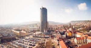 Blick auf einen Platz in einer Stadt mit einem großen runden Turm in der Mitte, vielen anderen Gebäuden und einem Parkplatz
