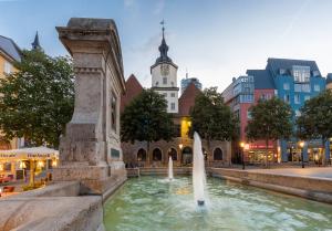 Bismarktbrunnen mit zwei Wasserfontänen, dahinter das Rathaus mit einem spitzen Turm