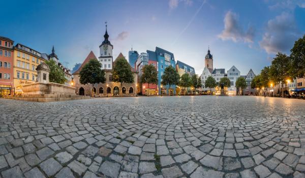Im Vordergrund Boden mit Plastersteinen, Hintergund Häuser des Jenaer Marktplatzes mit Rathaus, Bismarckbrunnen