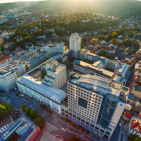 Blick auf den Jenaer Campus. Luftbildaufnahme mit Blick auf einen großen Gebäudekomplex mit Hochhäusern dahinter kleinere Häuser und Grün.