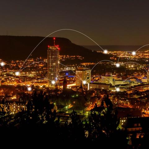 Jena bei Nacht mit Blick vom Landgrafen Richtung Süden. An verschiedenen Gebäuden sind kleine Leuchtpunkte hinzugefügt wurden, die mit ebenfalls leuchtenden Lichtbögen verbunden sind.