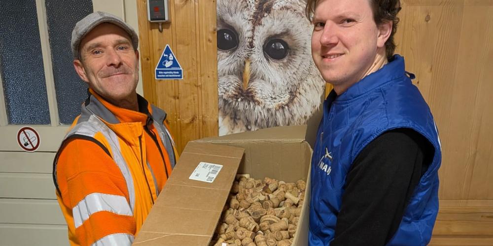 Zwei Männer halten eine Umzugskiste, die gefüllt ist mit Korken.