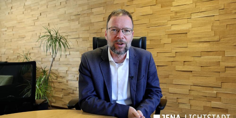 Ein Mann sitzt an einem Tisch und spricht direkt in eine Kamera.