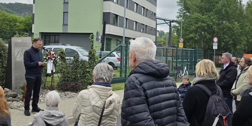 Oberbürgermeister Dr. Thomas Nitzsche steht an einem Mikrofon vor einer Gedenkstele, neben ihm ist ein Kranz aufgebaut, im Vordergrund stehen Zuhörerinnen und Zuhörer.