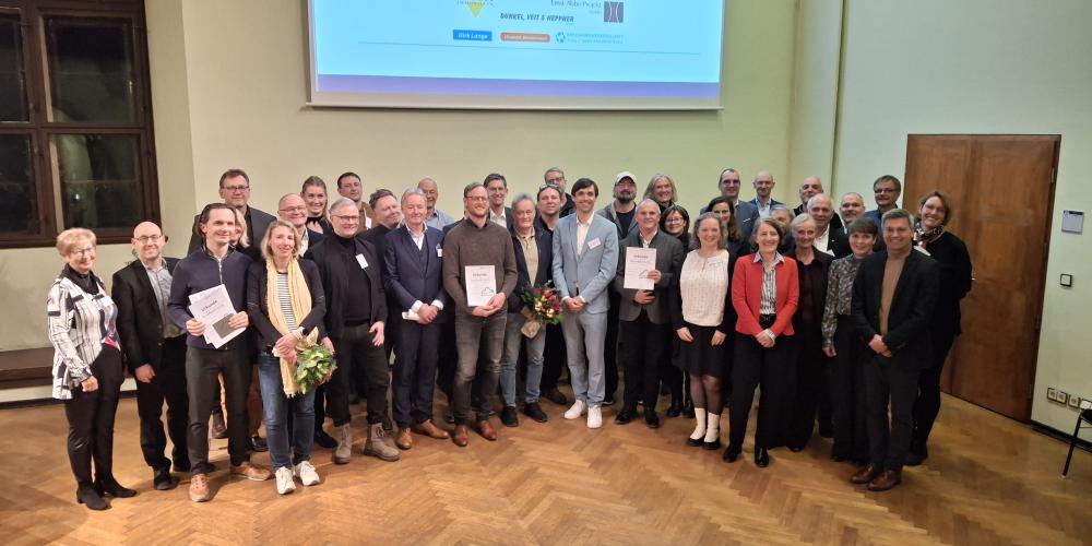 Gruppe von Menschen steht auf der Bühne und lacht in die Kamera.