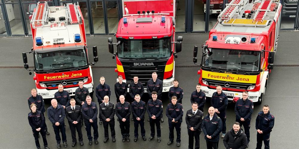 Feuerwehrleute stehen vor drei Autos und schauen in die Kamera.