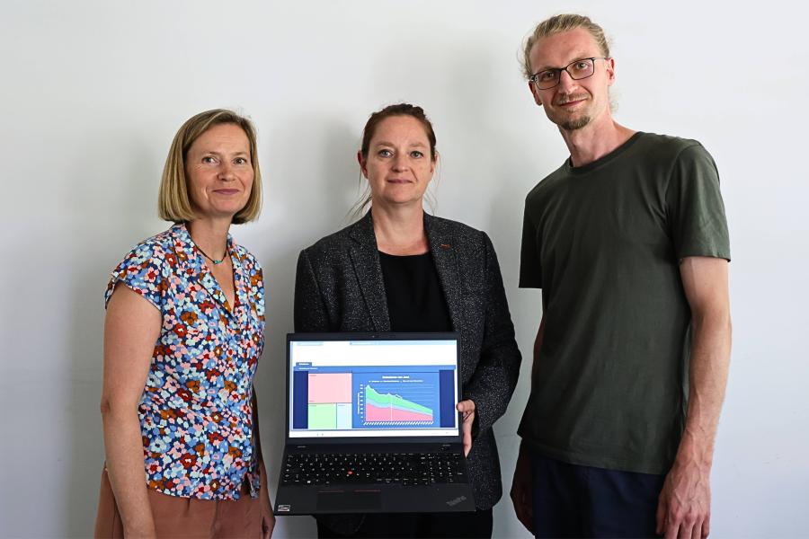 Zwei Frauen und ein Mann stehen nebeneinander. Eine Frau hält einen offenen Laptop, der das digitale Klimamonitoring der Stadt Jena zeigt.