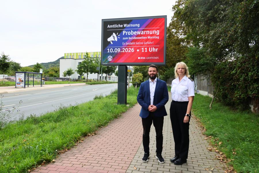 Ein Mann und eine Frau stehen vor einer digitalen Anzeigetafel in Jena.