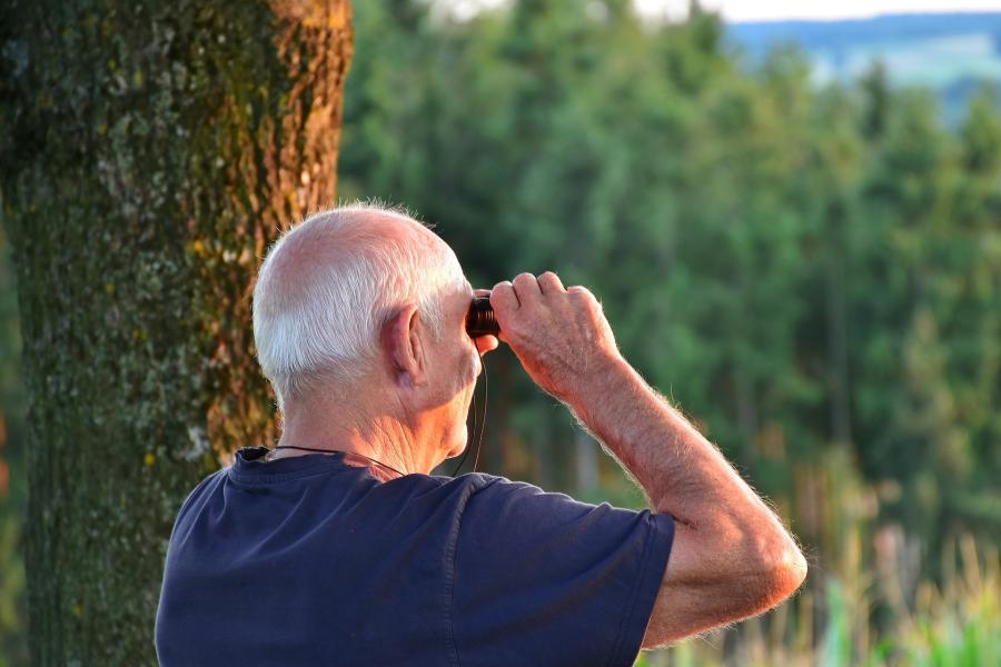 Ein Senior schaut durch ein Fernglas in die Weite