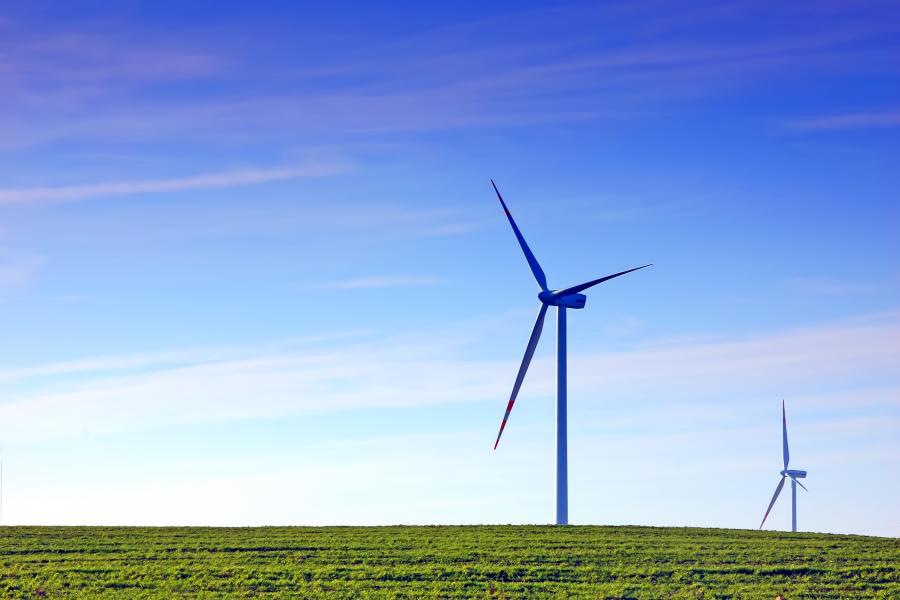 Zwei Windräder stehen auf einem grünen Feld.