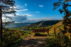 Eine Bank mit Blick auf ein Tal mit Häusern, am Horizont blauer Himmel