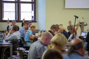 Blick in den Sitzungssaal einer Stadtratssitzung, Mitglieder heben Ihre Hände zur Abstimmung.