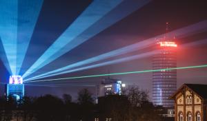 Laserstrahlen an einem Hochhaus strahlen in den Nachthimmel einer Stadt und auf ein weiteres Hochhaus