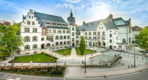 Blick von außen auf ein mehrteiliges Gebäude mit begrüntem Vorplatz