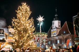 Blick auf den Jenaer Weihnachtsmarkt zu abendlicher Stunde, mit Weihnachtsbaum im Vordergrund, im Hintergrund Stände