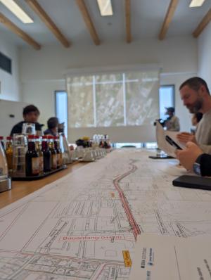 Mehrere Personen sitzen um einen Tisch herum, auf dem Kartenmaterial liegt.