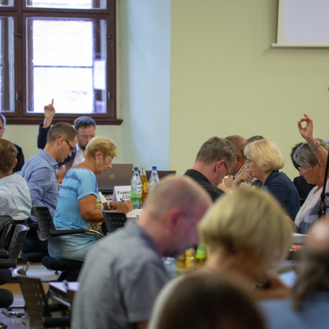 Blick in den Sitzungssaal einer Stadtratssitzung, Mitglieder heben Ihre Hände zur Abstimmung.