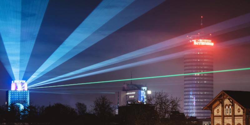 Laserstrahlen an einem Hochhaus strahlen in den Nachthimmel einer Stadt und auf ein weiteres Hochhaus
